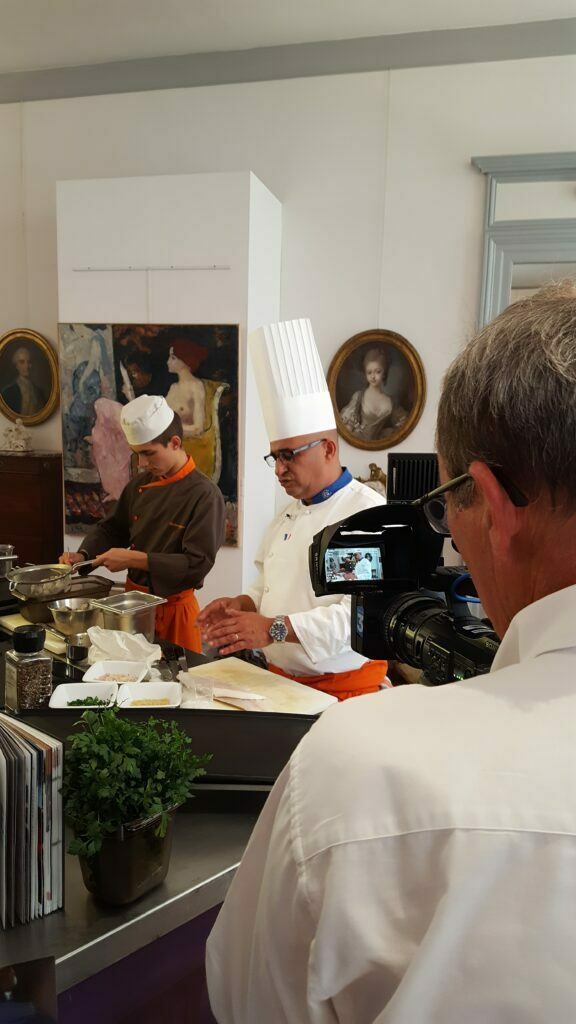 Chef et jeune apprenti en cuisine, filmés devant des portraits anciens au musée
