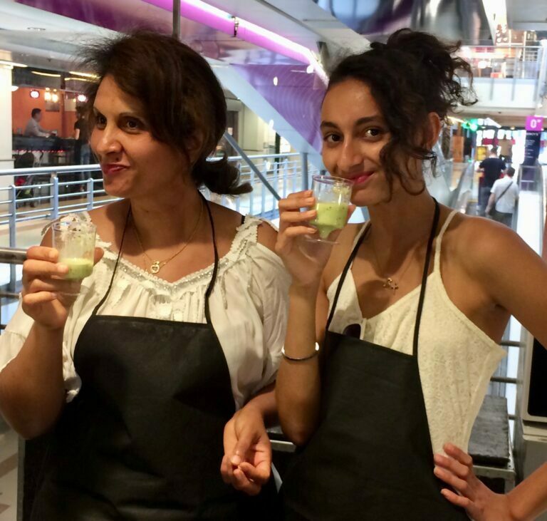 Deux femmes en tablier dégustent une verrine verte lors d'un événement