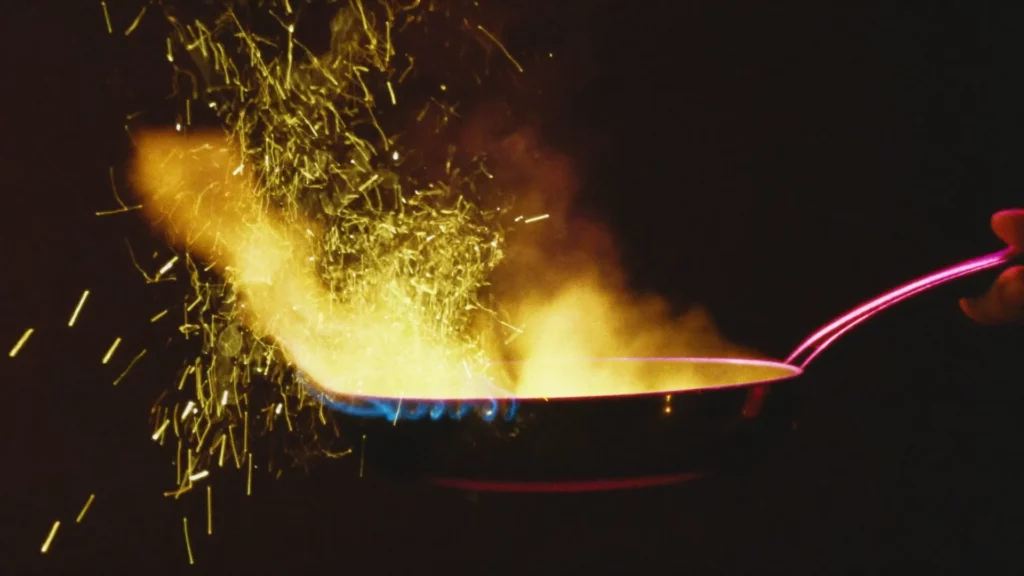 Flambage spectaculaire en gros plan lors d'un show culinaire Flyin'Chef : flammes et gerbe d'étincelles dans la pénombre