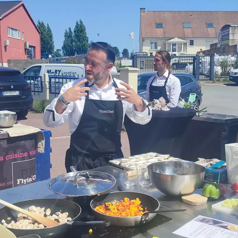 Chef Flyin'Chef animant un atelier culinaire sur une cuisine mobile installée en extérieur, sur un parking d'entreprise