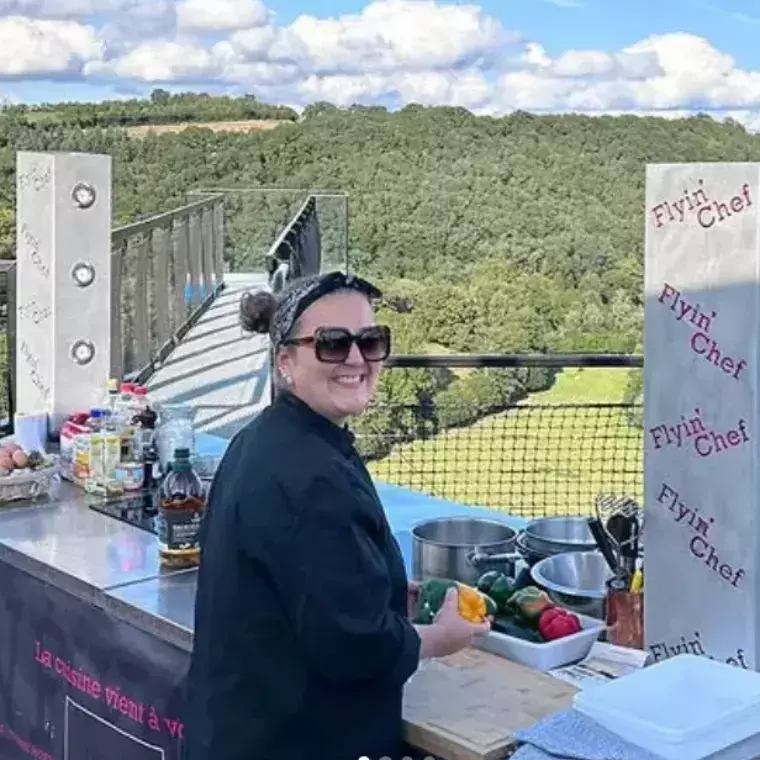Cheffe Flyin'Chef cuisinant en plein air sur une passerelle suspendue au-dessus d'une vallée