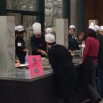 Participants en toque répartis par équipes autour des plans de travail d'un team building culinaire
