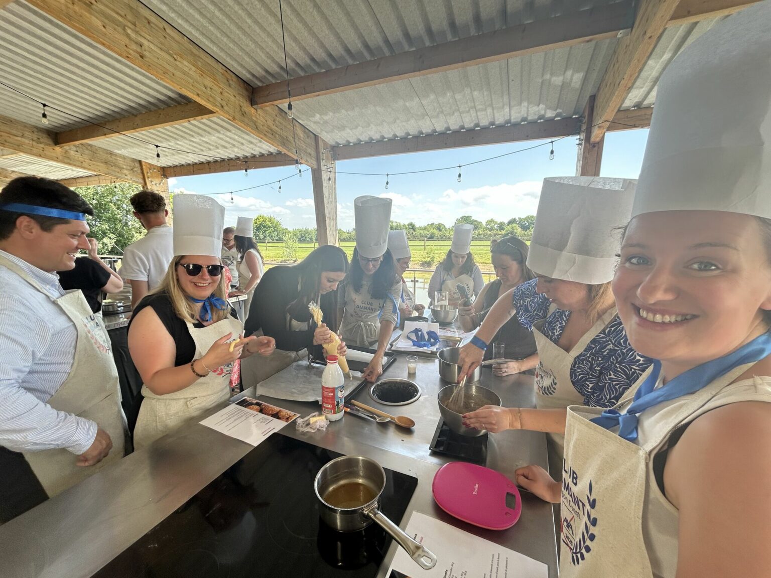 Groupe de participants en toques et tabliers cuisinant sous un préau pendant un team building culinaire