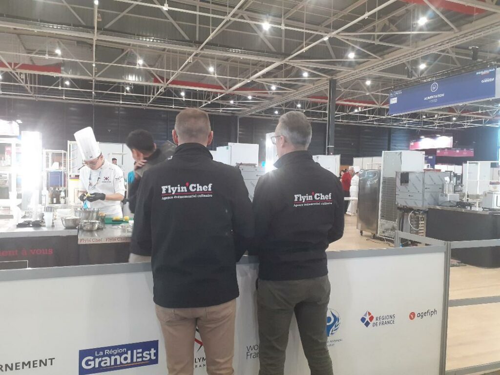 Deux membres de l'équipe Flyin'Chef en veste logotée devant un candidat des Abilympics internationaux à Metz
